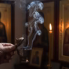 amber-incense-in-use-censing A person's hand gently censing a home prayer corner with a bronze katzion, with a thick plume of smoke rising before a candlelit icon.