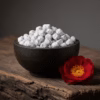 A dark soapstone bowl of handcrafted Wild Rose incense from the Treasury Collection, with a single, deep crimson wild rose beside it.