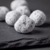A macro, close-up shot of hand-cut Wild Rose incense, showing its magnesia coating and handcrafted texture on a dark slate surface.