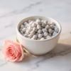 A white ceramic bowl of handcrafted Rose incense, with a beautiful, fresh, pink rose on a white marble surface.