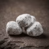 An extreme macro shot of hand-cut Nard incense pieces, showing the texture and magnesia coating on a rough, dark stone surface.